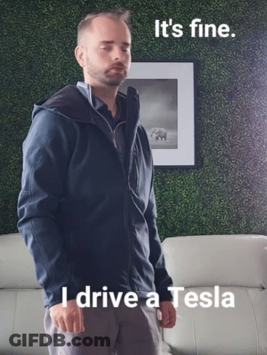 A Man In A Blue Jacket Is Standing In Front Of A Picture That Says I Drive A Tesla GIF