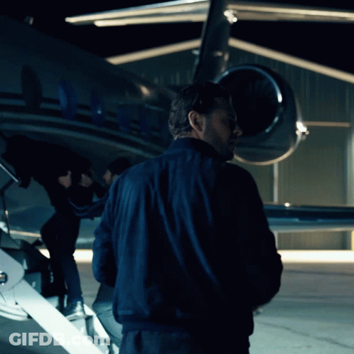 A Man In A Blue Jacket Is Standing In Front Of A Plane With The Letters Aa On The Tail GIF