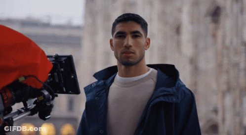 A Man In A Blue Jacket Is Standing In Front Of A Red Camera GIF