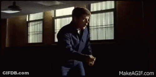 A Man In A Blue Jacket Is Standing In Front Of A Window In A Room . GIF