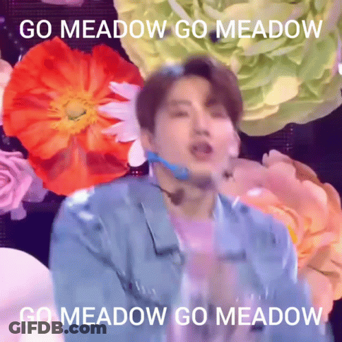 A Man In A Blue Jacket Is Standing In Front Of Flowers With The Words Go Meadow Go Meadow GIF
