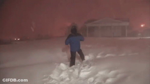 A Man In A Blue Jacket Is Standing In The Snow In Front Of A House GIF