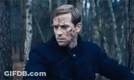 A Man In A Blue Jacket Is Standing In The Woods With Blood On His Face . GIF