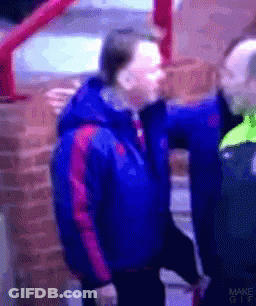 A Man In A Blue Jacket Is Standing Next To Another Man GIF