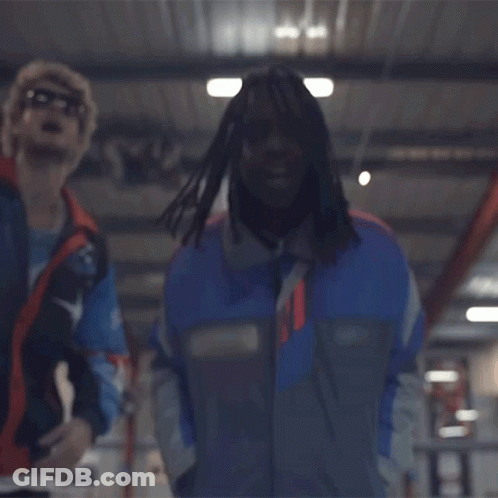 A Man In A Blue Jacket Is Standing Next To Another Man In A Red Vest . GIF