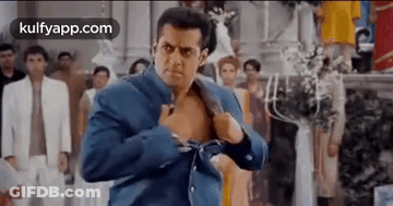 A Man In A Blue Jacket Is Taking Off His Shirt . GIF