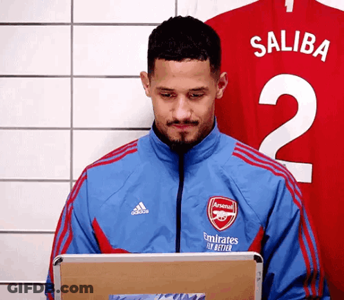 A Man In A Blue Jacket Is Using A Laptop In Front Of A Red Jersey . GIF
