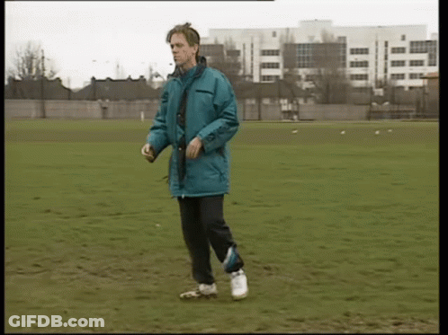 A Man In A Blue Jacket Is Walking On A Grassy Field GIF
