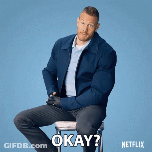 A Man In A Blue Jacket Sits On A Stool With Okay Written On The Bottom GIF