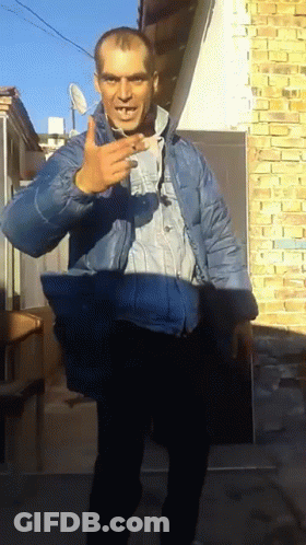 A Man In A Blue Jacket Stands In Front Of A Brick Building GIF