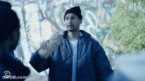 A Man In A Blue Jacket Stands In Front Of A Graffiti Wall With A Copyright Symbol GIF