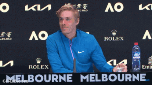 A Man In A Blue Jacket Stands In Front Of A Melbourne Banner GIF