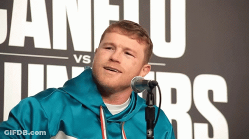 A Man In A Blue Jacket Stands In Front Of A Microphone In Front Of A Sign That Says Vs Juniors GIF