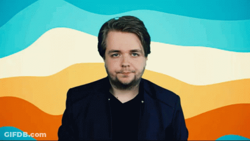 A Man In A Blue Jacket Stands In Front Of A Rainbow Colored Background GIF