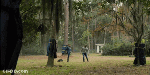 A Man In A Blue Jacket Stands In The Middle Of A Grassy Field In The Woods GIF