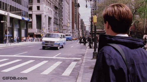 A Man In A Blue Jacket Stands On The Sidewalk Looking At A Crosswalk GIF