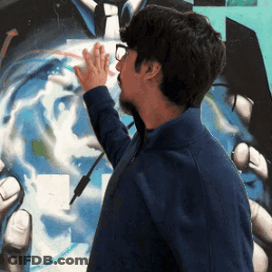 A Man In A Blue Jacket Touches A Painting Of A Man In A Suit And Tie GIF