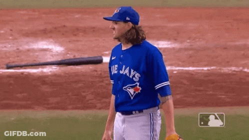 A Man In A Blue Jays Jersey Is Standing On A Baseball Field With A Bat In The Background . GIF