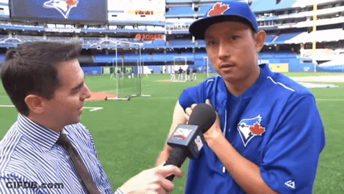 A Man In A Blue Jays Uniform Is Being Interviewed By A Reporter GIF
