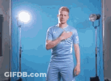 A Man In A Blue Jersey Is Standing In Front Of A Blue Background . GIF