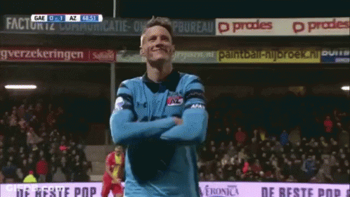 A Man In A Blue Jersey Is Standing In Front Of A Sign That Says " De Beste Pop " GIF
