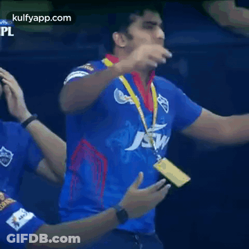 A Man In A Blue Jersey With A Medal Around His Neck Is Standing In Front Of A Crowd . GIF