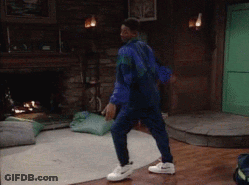 A Man In A Blue Jumpsuit And White Nike Shoes Is Dancing In A Living Room GIF