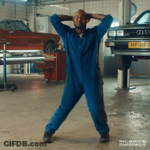 A Man In A Blue Jumpsuit Is Dancing In Front Of An Audi Car GIF