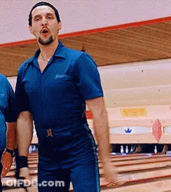 A Man In A Blue Jumpsuit Is Standing On A Bowling Alley GIF