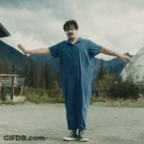 A Man In A Blue Jumpsuit Is Standing With His Arms Outstretched . GIF