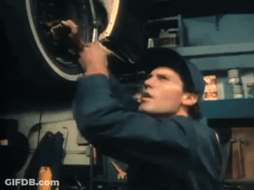 A Man In A Blue Jumpsuit Is Working On A Car GIF