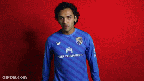 A Man In A Blue Kaiser Permanente Jersey Holds Up A Book GIF