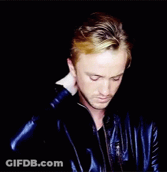 A Man In A Blue Leather Jacket Holds His Hand To His Head GIF