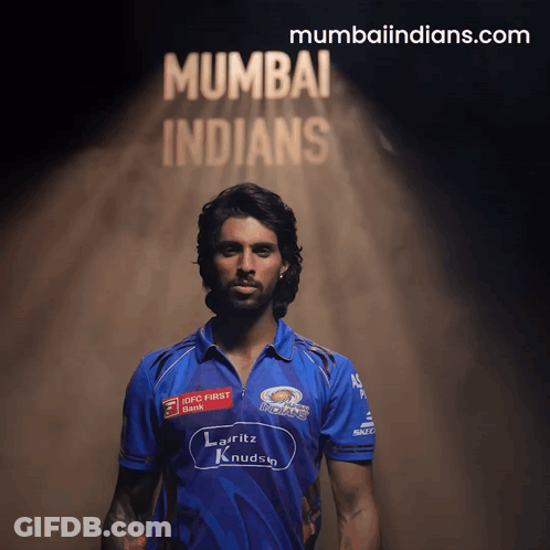 A Man In A Blue Mumbai Indians Jersey Stands In Front Of A Sign That Says Mumbaiindians.com GIF