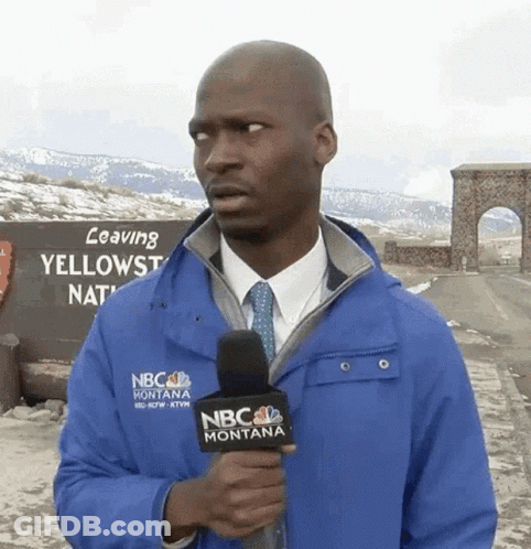 A Man In A Blue Nbc Montana Jacket Holds A Microphone In Front Of A Sign That Says Leaving Yellowstone National Park GIF