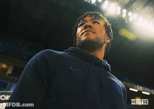 A Man In A Blue Nike Hoodie Stands In A Dark Room With Chelsea Written On The Bottom GIF