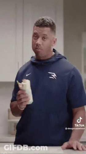 A Man In A Blue Nike Shirt Holds A Burrito In His Hand GIF