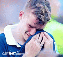 A Man In A Blue Nike Shirt Is Crying With His Hands On His Face . GIF