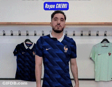 A Man In A Blue Nike Shirt Is Standing In Front Of A Sign That Says Rayan Cherki GIF