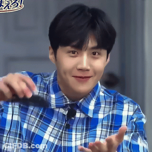 A Man In A Blue Plaid Shirt Is Smiling And Holding Something GIF