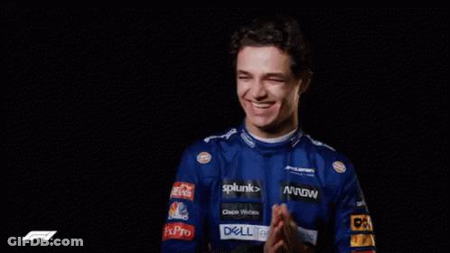 A Man In A Blue Racing Uniform Is Smiling And Clapping His Hands . GIF