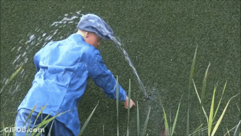 A Man In A Blue Raincoat Is Spraying Water From A Hose . GIF