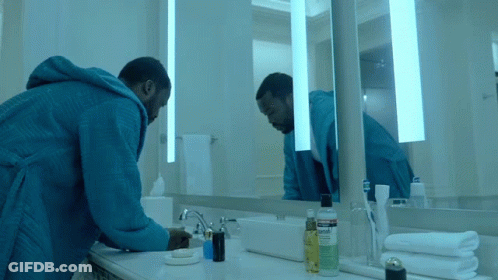 A Man In A Blue Robe Is Looking At Himself In The Mirror GIF