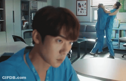 A Man In A Blue Scrub Is Looking At Another Man In A Blue Scrub In A Living Room GIF
