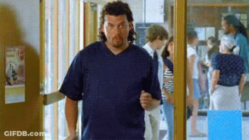 A Man In A Blue Scrub Top Is Standing In A Hallway With People Behind Him . GIF
