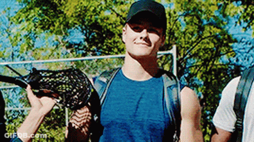 A Man In A Blue Shirt And Black Hat Is Holding A Lacrosse Stick In His Hand . GIF