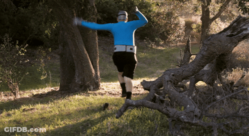 A Man In A Blue Shirt And Black Shorts Is Running Through A Forest GIF