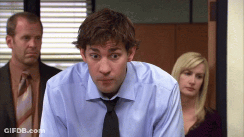A Man In A Blue Shirt And Black Tie Looks At The Camera GIF