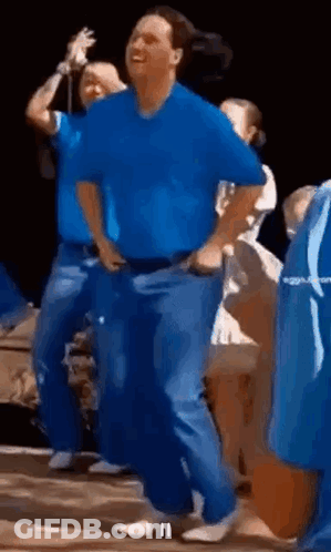 A Man In A Blue Shirt And Blue Jeans Is Dancing In A Crowd . GIF