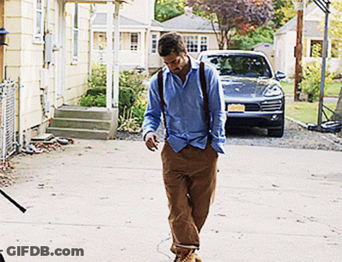 A Man In A Blue Shirt And Brown Pants Is Walking In Front Of A Car With A License Plate That Says N.j. GIF